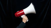 Hand holding red and white megaphone against dark background, suitable for announcement, promotion, marketing campaigns, and communication concepts.