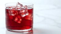 Red cocktail drink with ice cubes in a glass on a marble surface, refreshing beverage concept for menu, bar, and restaurant use.