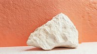 Raw white limestone or chalk mineral specimen on coral background with harsh shadow, minimalist geological composition for educational and design purposes.