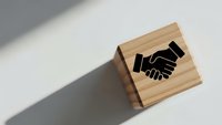 Wooden rubber stamp with handshake icon on white surface with shadow. Business partnership agreement seal for contracts and documents.