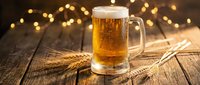 Fresh golden beer mug with foam on rustic wooden table with wheat stalks and warm bokeh lights creating cozy pub atmosphere for brewing concepts.