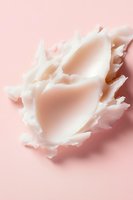 Delicate white cream swirl floating on soft pink background with gentle shadows creating ethereal mood, suitable for beauty and skincare advertising.