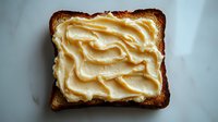 Creamy peanut butter spread on toasted whole grain bread slice, breakfast food concept for healthy morning meal and snack preparation on white background.