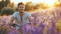 Young Caucasian man with beard smiling while riding bicycle through blooming lavender field at golden sunset hour, wearing casual summer clothing for lifestyle and wellness concepts.