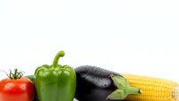 Fresh organic vegetables including ripe tomato, green bell pepper, eggplant and corn cob arranged on white background for healthy cooking and nutrition.