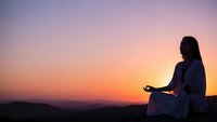 Woman meditating at sunset with peaceful sky gradient. Silhouette practicing mindfulness and yoga outdoors during golden hour for wellness and relaxation.