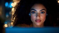 Young African American woman illuminated by blue screen light in dark room with bokeh background, wearing professional makeup and natural curly hair.