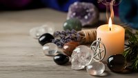 Spiritual healing crystals with burning candle and pentagram pendant on wooden surface for meditation, energy cleansing and mystical practices.