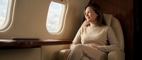 Young woman relaxing in luxury private jet cabin wearing beige sweater looking out window during flight for business travel and lifestyle content.