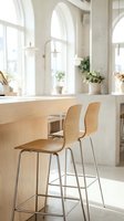 Bright modern kitchen interior with wooden bar counter, two contemporary bar stools with metal legs, and abundant natural light streaming through arched windows with potted plants on sills.