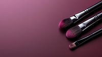 Professional makeup brushes with soft synthetic bristles arranged on burgundy background with copy space for beauty and cosmetic industry marketing.
