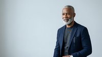Mature African American male professional wearing navy blazer and gray shirt, smiling at camera against white background for corporate portraits and business headshots.