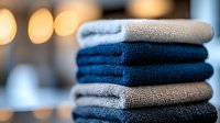 Stack of folded navy blue and gray cotton towels with soft bokeh background, arranged in alternating colors for spa, bathroom, or hotel amenities display.