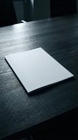 Blank white paper sheet on dark wooden desk with dramatic lighting for business presentations and corporate branding mockups.
