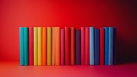 Row of colorful hardcover books standing in line against vibrant red background, creating rainbow gradient effect from turquoise through yellow to deep blue tones.