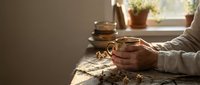 Elderly hands holding warm tea cup in cozy morning light with rustic wooden table setting and peaceful home atmosphere for relaxation and comfort.
