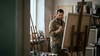 Middle-aged Caucasian male artist painting on canvas in bright art studio workspace with easels and creative supplies for artistic projects.
