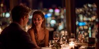 Young couple enjoying romantic dinner date at upscale restaurant with city lights bokeh background, intimate evening dining experience for anniversary celebration.