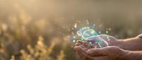 Hands holding glowing globe with digital particles and light effects, representing global connectivity, technology innovation, and environmental sustainability concepts.