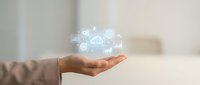 Hand holding holographic cloud computing icons with data analytics symbols floating above palm in modern office environment for digital transformation.
