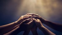 Diverse hands joining together in unity and teamwork against warm golden light background symbolizing collaboration, support and community connection.