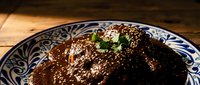 Rich chocolate mole sauce with sesame seeds and fresh herbs on decorative ceramic plate, traditional Mexican cuisine for restaurant menus and culinary content.