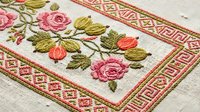 Traditional floral embroidery with pink roses and green leaves on linen fabric featuring decorative geometric border pattern for textile crafts and needlework.