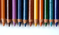 Colorful wooden pencils arranged in row on white background, sharp tips aligned, showing vibrant spectrum of colors for art and education concepts.