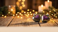 Purple heart-shaped Christmas ornaments with golden string lights on rustic wooden surface creating warm festive holiday atmosphere for seasonal decorating.