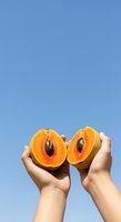 Hands holding halved apricot with pit visible against clear blue sky, showcasing fresh fruit and natural food for healthy eating, nutrition, and summer produce concepts.