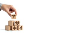 Hand placing wooden cube with medical caduceus symbol onto stack of healthcare blocks on white background for design projects.