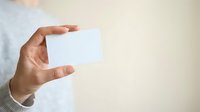 Close-up of male hand holding blank white business card against neutral beige background, suitable for corporate branding and professional identity design.