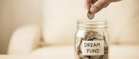 Hand dropping coin into glass jar labeled dream fund, representing savings, financial goals, and investment in future aspirations.