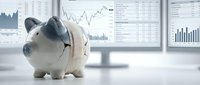 Piggy bank with graduation cap on desk with financial charts and graphs displayed on computer monitors in background for education savings planning.