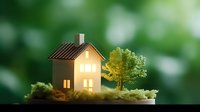 Miniature glowing house model with illuminated windows and tiny tree on moss platform against blurred green bokeh background, creating cozy home atmosphere.