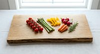Fresh colorful vegetables arranged on rustic wooden cutting board including cherry tomatoes, asparagus, carrots, bell peppers and radishes for healthy cooking.