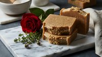 Handmade natural soap bars stacked on marble with fresh red rose and herbs, showcasing organic skincare products for wellness and beauty routines.