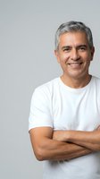 Confident mature Hispanic man with gray hair smiling with crossed arms in white t-shirt on neutral background for lifestyle and wellness content.