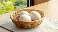 Fresh white chicken eggs in woven bamboo basket on linen napkin near window with natural daylight and green bokeh background.