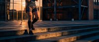 Young professional woman walking down concrete steps in warm golden hour light outside modern office building during sunset commute.
