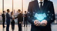 Professional businessman in suit holding glowing digital handshake hologram with network icons in modern office with team meeting in background.