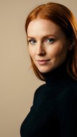 Portrait of confident young Caucasian woman with red hair and blue eyes wearing black turtleneck sweater against neutral beige background for business.
