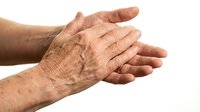 Elderly person with wrinkled skin showing age spots and signs of aging on hands and forearms against white background for healthcare and dermatology concepts.