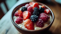 Fresh mixed berries with strawberries, raspberries and blackberries served on creamy yogurt in brown ceramic bowl, close up view on wooden table.