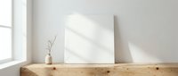 Minimalist interior with blank white canvas on wooden shelf near window with natural sunlight creating soft shadows on wall for mockup display.