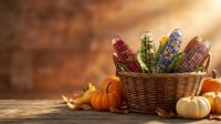 Colorful corn cobs in wicker basket with autumn pumpkins and leaves on rustic wooden table for seasonal harvest decoration and thanksgiving celebration.