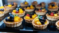 Fresh fruit tartlets with golden mango, blueberries, and strawberries arranged on black surface, topped with glazed berries and mint garnish in flaky pastry shells.