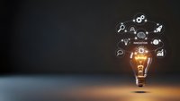 Glowing light bulb with innovation icons floating above on dark background representing creative ideas, brainstorming and business solutions for marketing.
