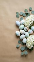 Pastel Easter eggs with white hydrangea flowers and eucalyptus leaves arranged on beige background for spring holiday celebration and greeting cards.