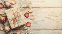 Vintage gift box wrapped in craft paper with dried rose petals scattered on rustic wooden background for romantic occasions and special celebrations.